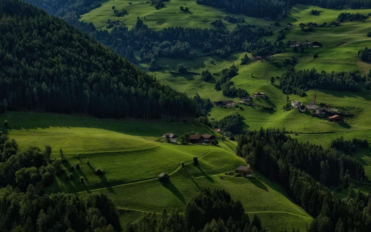 https://www.pexels.com/photo/a-small-town-on-the-green-grass-field-6055472/ Pogled na brdoviti kraj sa proplancima, šumom i kućama